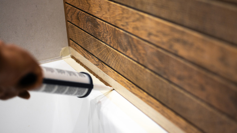 Hand installing caulking on edge of tub