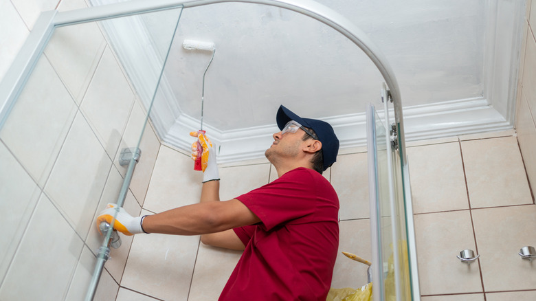 man painting the ceiling over a shower