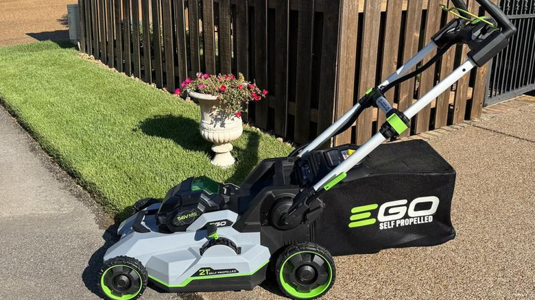 Brand new Ego push mower on walkway beside manicured lawn and flower pot