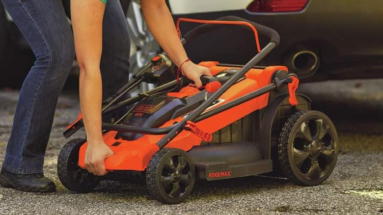 Someone packing up an orange Black+Decker lawn mower