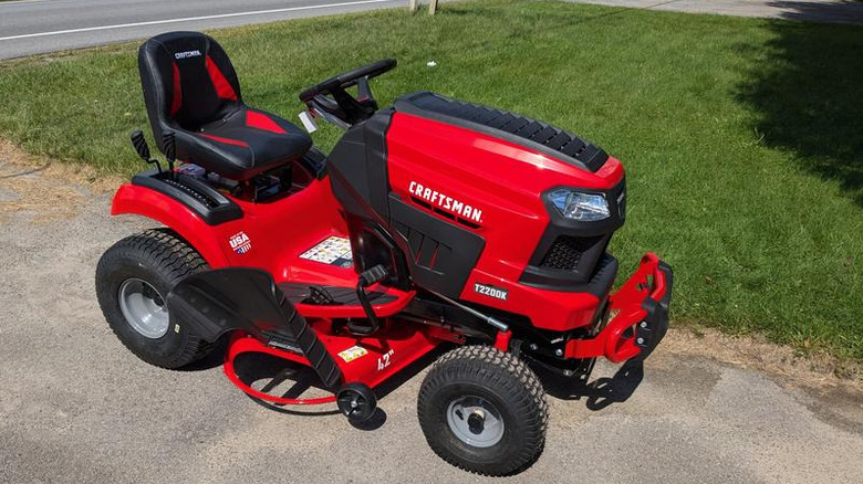 Red Craftsman riding lawn mower on a driveway beside a manicured lawn