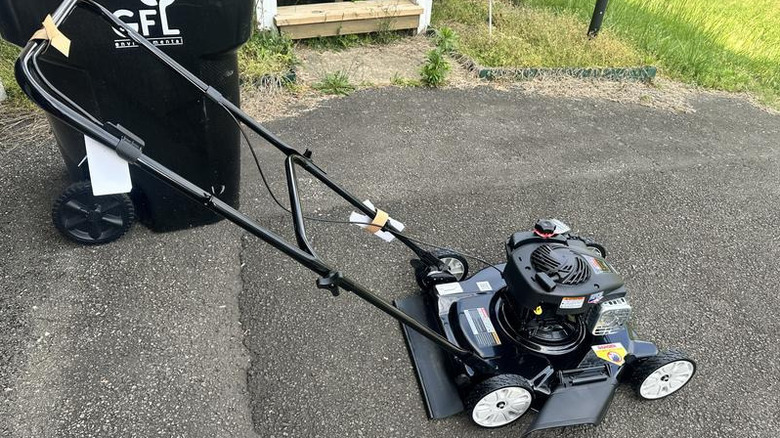 Black Murray push mower on asphalt driveway by a garbage can