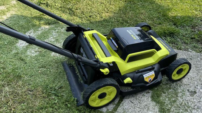 Green Ryobi mower on stone path surrounded by grass clippings