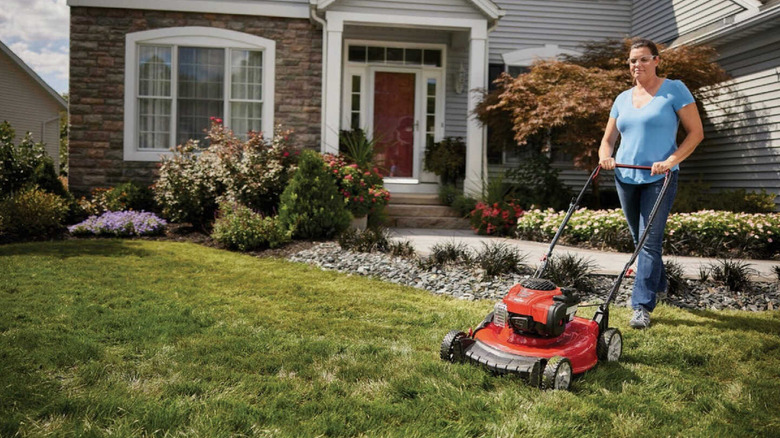 Red Troy-Bilt gas push mower on mowed lawn by outdoor seating area