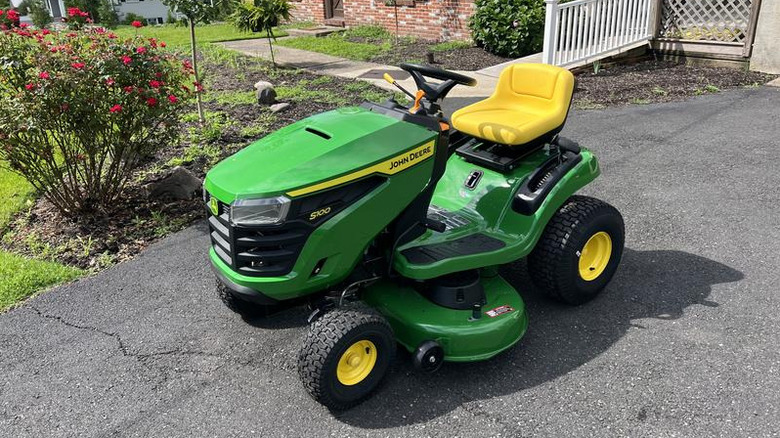 Green John Deere riding lawn mower outside home on asphalt driveway