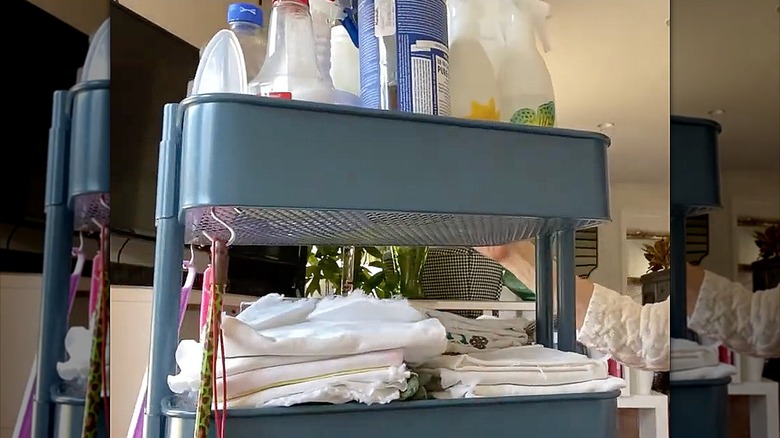 A blue IKEA cart with cleaning bottles on the top and rags on the middle rack