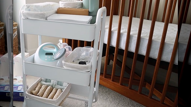 White RASKOG cart full of baby supplies next to crib