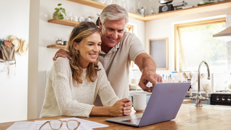 Happy couple browsing laptop in stylish kitchen
