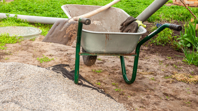 Wheelbarrow with shovel and gloves next to a pile of gravel