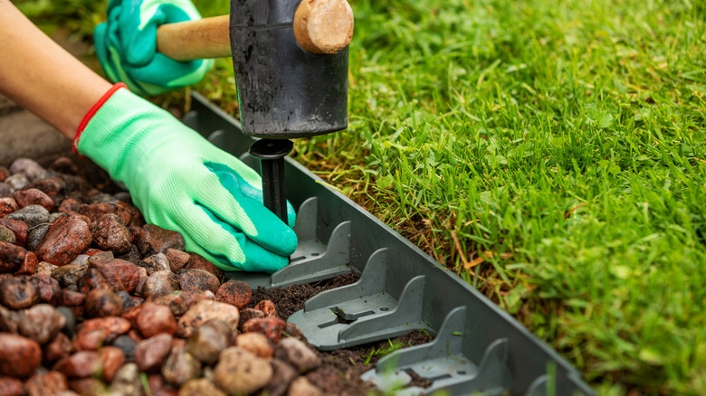 Person installing plastic landscape edging by pounding pegs into the ground