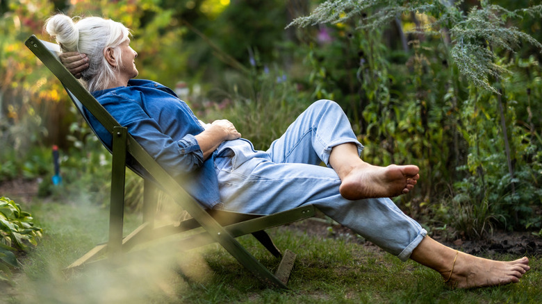 A woman with gray hair relaxing in a chair in her garden.