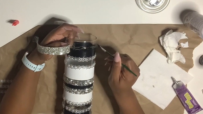 Woman painting glass cylinder vase with glitter ribbon and other arts and crafts materials