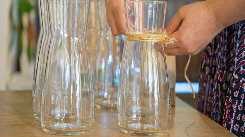 Woman tying twine string around unique glass vase on wood table