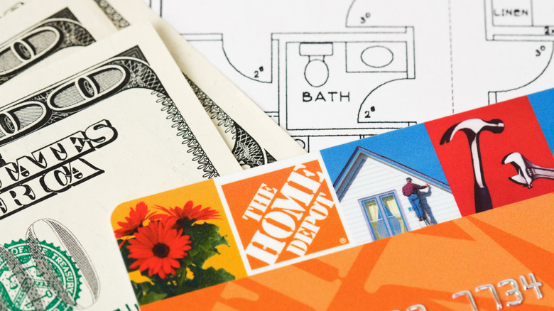 The corner of a Home Depot credit card and 100 dollar bills.