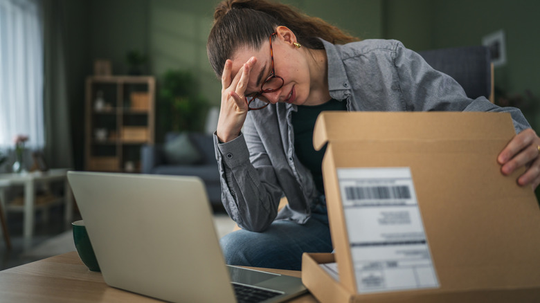 A woman with her head in her hands and a cardboard package.