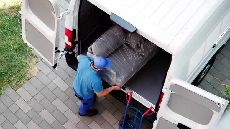 A man unloading a gray sofa from a truck.
