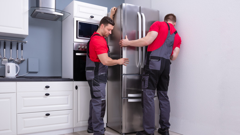 Two men installing a stainless steel refrigerator.