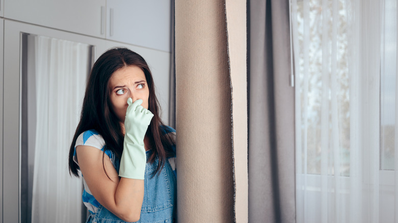 A woman holding her nose and a smelly rug.