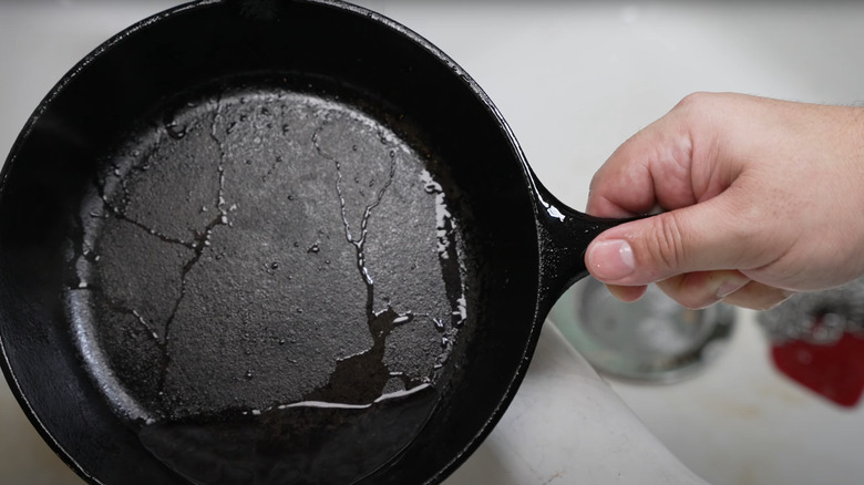 Hand holding washed cast iron pan dripping with water