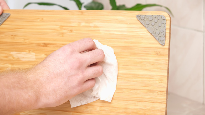 Hand wiping down wood cutting board with soft tissue