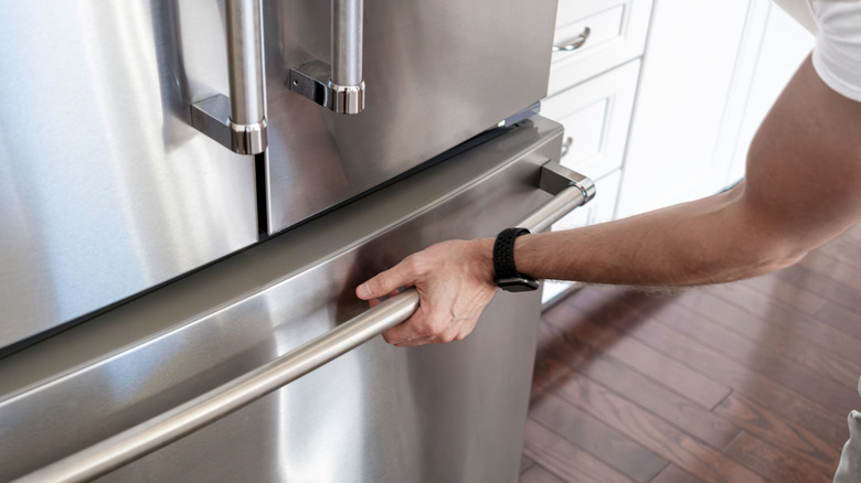 A man opens a stainless steel fridge