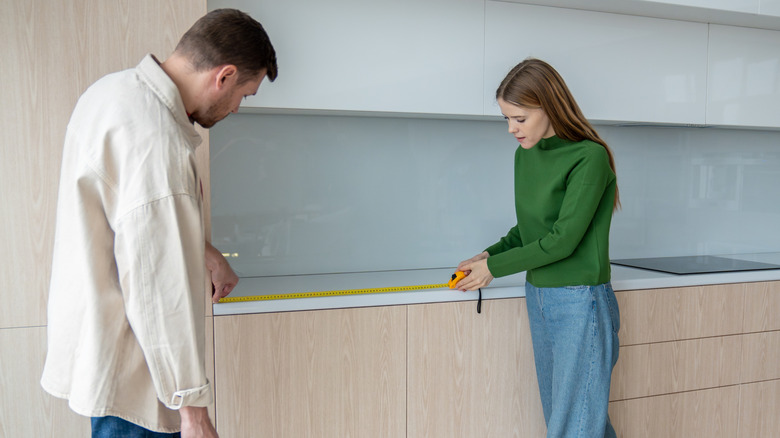 Two people measuring a kitchen countertop