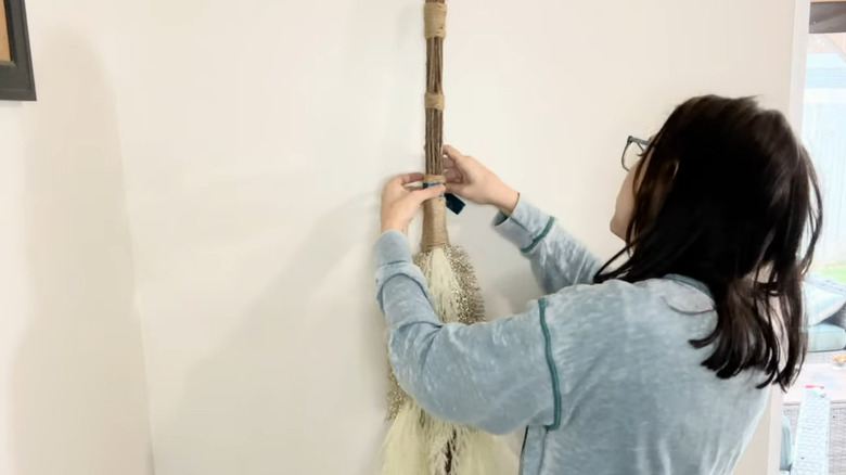 Person attaching pampas grass fronds to hanging cinnamon broom