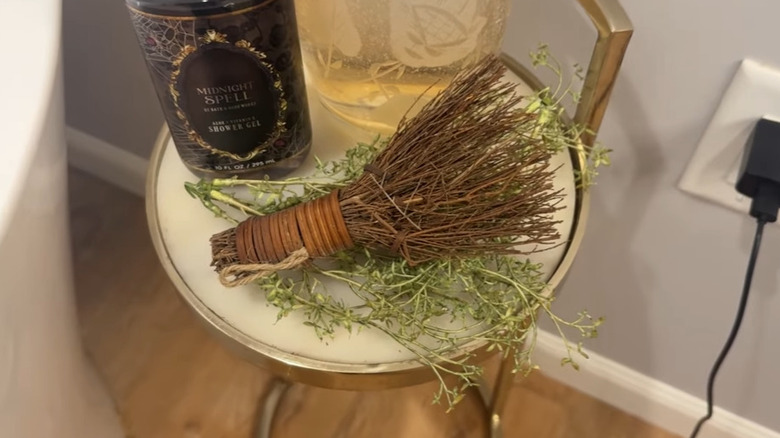 Mini cinnamon broom sitting on top of dried greenery next to candles