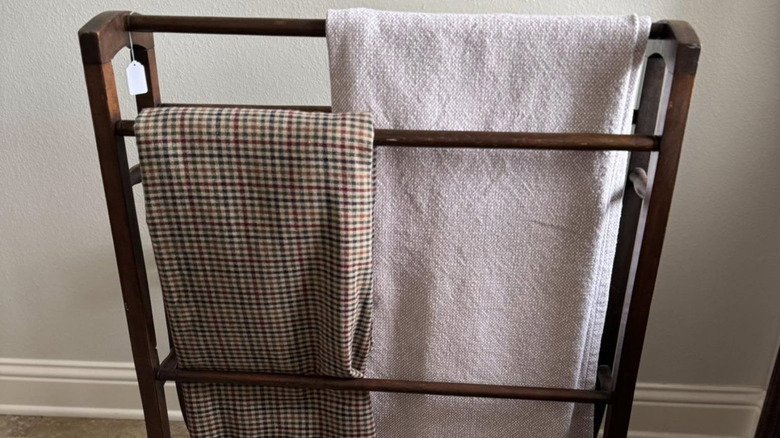 Dark wood quilt rack with paper price tag holding two blankets, one a checkered and one a solid pink