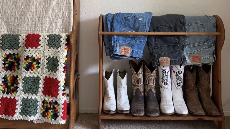 Wooden quilt rack repurposed to display three pairs of jeans and four pairs of cowboy boots next to another quilt rack with afghan