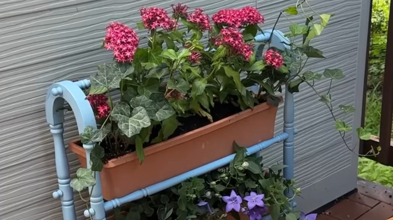 Blue quilt rack made into a planter with planter boxes holding array of flowers on a porch
