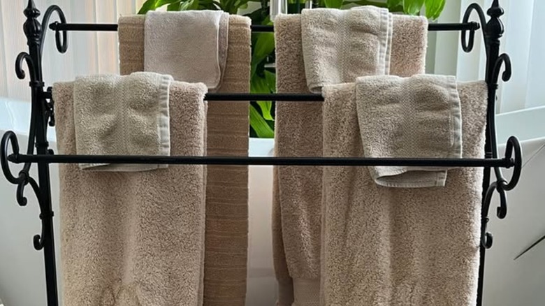 Off-white towels hanging on black metal quilt rack in front of a plant