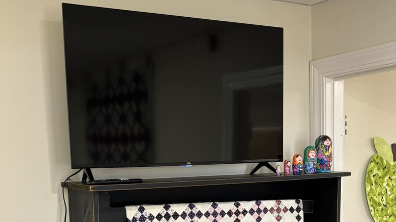 TV set atop a wooden quilt rack mounted to the wall, a set of nesting dolls and a hanging quilt on the rack as well