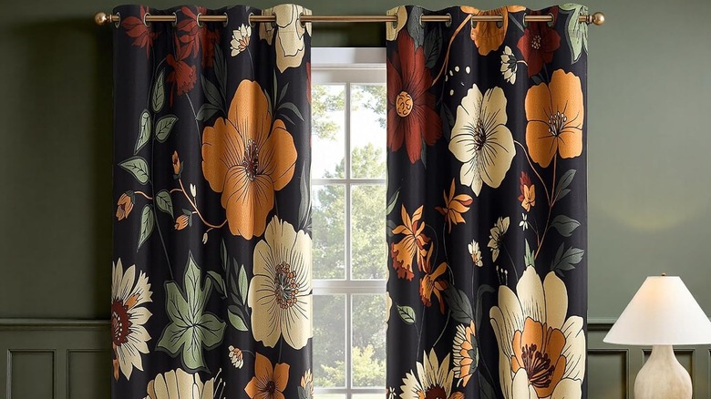 Sage green walls and a window dressed with black, orange, yellow, red, and cream floral curtains.