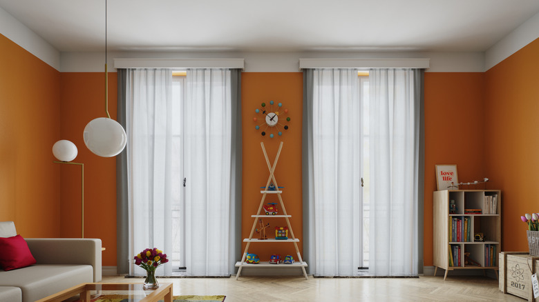 An orange-walled living room with light gray curtains and neutral-hued furniture.