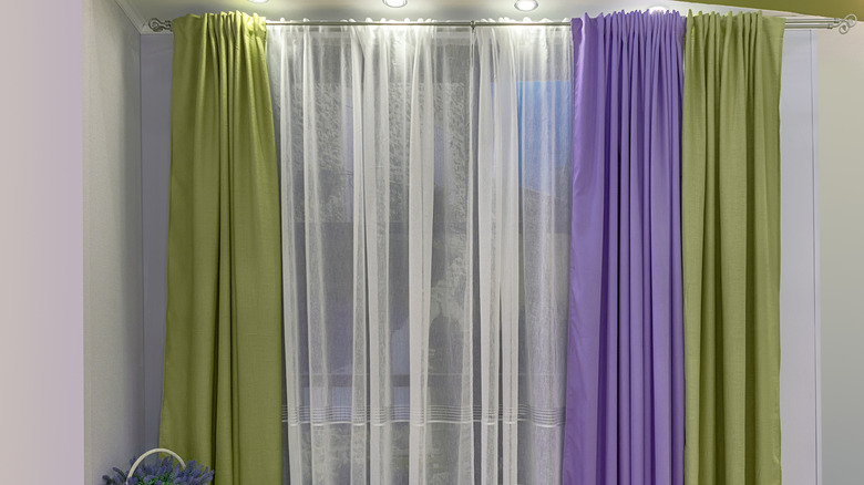 Bright lavender, lime green, and sheer white curtains dress a window in a room with off-white walls.