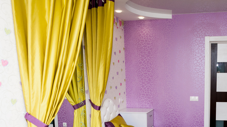 A bold purple accent wall and sunshine yellow curtains in a bedroom.