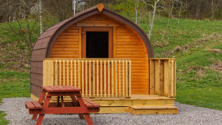 A tiny arched cabin made of wood sitting on a rubble foundation.