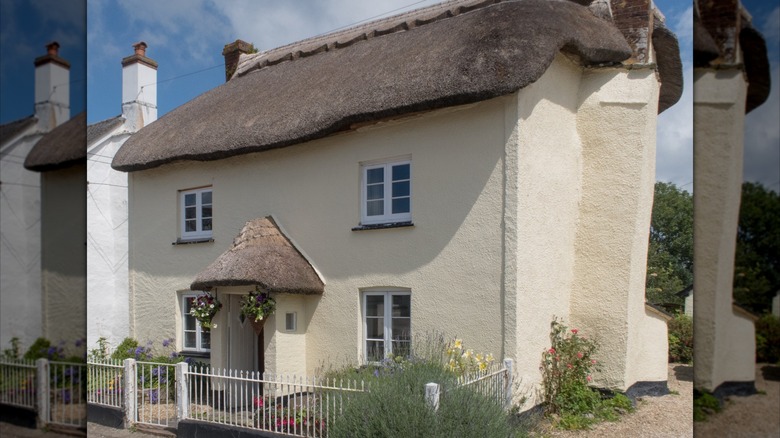 A butter yellow colored cob cottage with thatched roof.