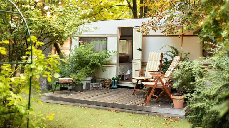 A converted airstream camper with a front deck porch and stringed lights above it.