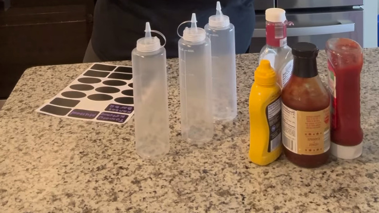 Three condiment bottles sitting next to a selection of sauce bottles and labels on a counter.