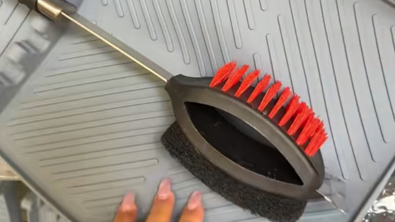 A hand resting on a silicon mat next to a grill cleaner.