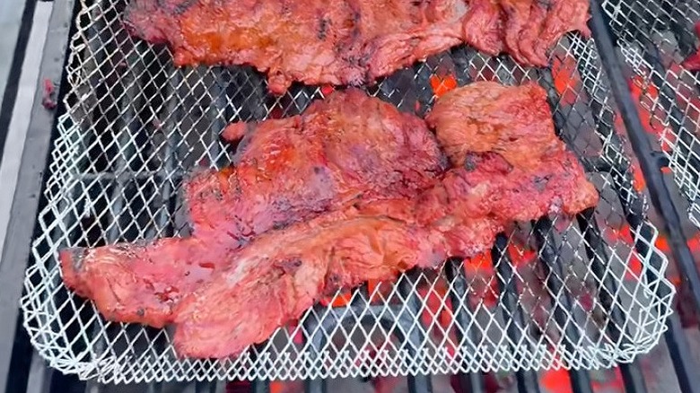 Meat grilling over a grill tray on a charcoal grill.