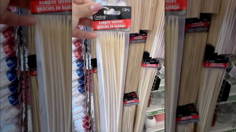 A hand holds a packet of bamboo skewers in front of a display wall at Dollar Tree.