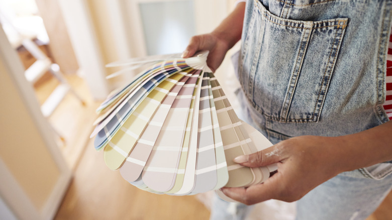 A woman in overalls looking at paint swatches.