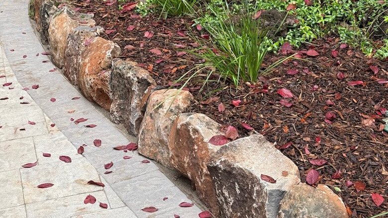 Boulders separate a driveway from a garden bed.