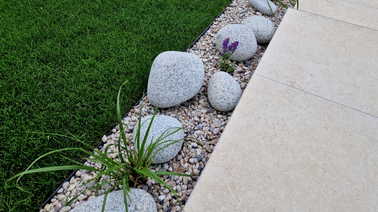 Driveway is bordered with large river rocks, pebbles, and plants.