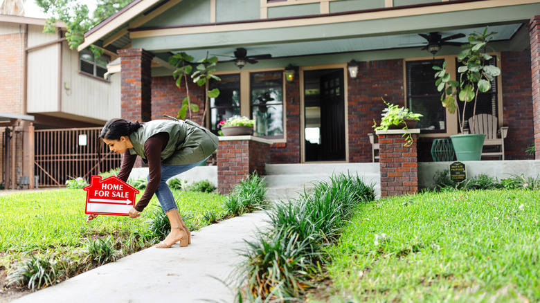 person putting for sale sign in front of brick home