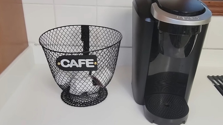 Mug-shaped basket holding K-cups next to a Keurig machine on a white countertop