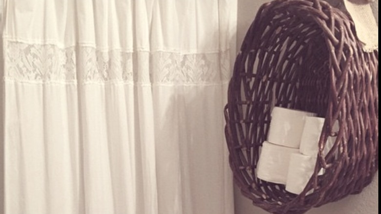 A basket hanging on the wall with toilet paper inside